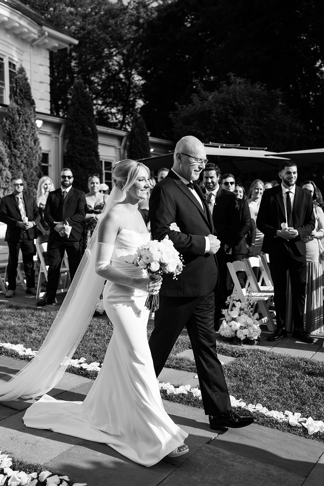 Black and white photo of the bride and her father smiling as they walk down the aisle during the ceremony.